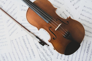 overhead picture of a violin facing diagonally with bow, on top of a pile of sheet music